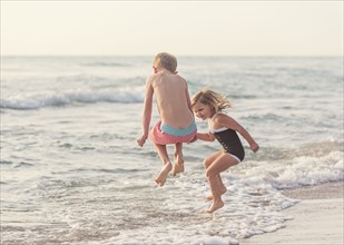 Boy (6-7) and girl (4-5) jumping in water on beach