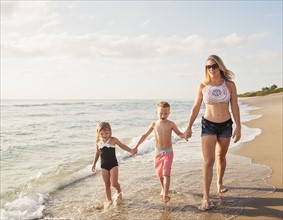 Mother walking with boy (6-7) and girl (4-5) on beach by water