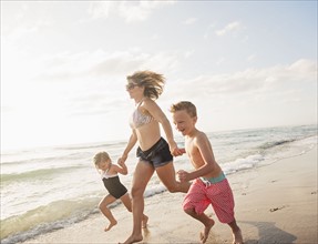 Mother running with boy (6-7) and girl (4-5) on beach by water