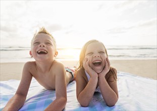 Boy (6-7) and girl (4-5) lying on beach laughing