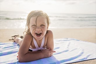 Girl (4-5) lying on beach laughing