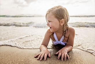Girl (4-5) lying down in water on beach