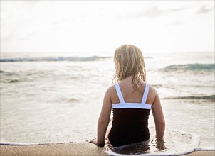 Girl (4-5) lying down in water on beach