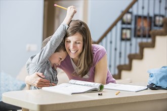 Smiling mother hugging son (6-7) doing homework