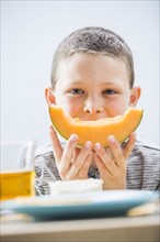 Little boy (6-7) eating cantaloupe for breakfast