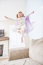 Little girl (4-5) playing superhero on sofa