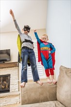Boys (2-3, 6-7) wearing superhero costumes standing on sofa