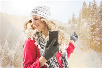 Young woman wearing winter clothing dancing with smart phone in hands