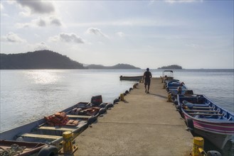 Man walking along pier with boats moored along