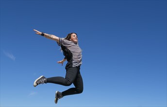 Young woman jumping against clear sky.