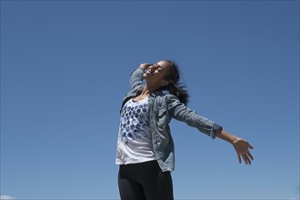 Mid adult woman outstretching her arms against blue sky.