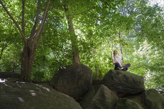 Young woman meditating on rocks in woodland.