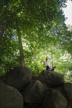 Young woman meditating on rocks in woodland.