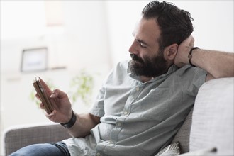Mid-adult man using smartphone on couch.