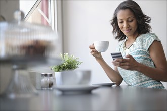 Woman drinking coffee and using phone.