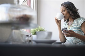 Woman drinking coffee and using phone.