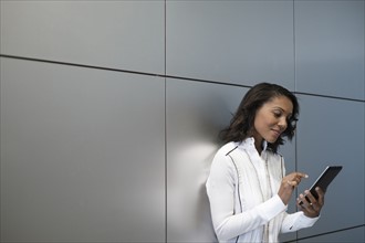 Woman standing by wall and using digital tablet.
