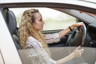 Woman with curly, long, blond hair driving car.