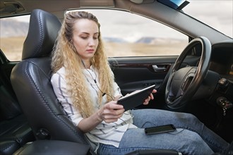Woman sitting in car and using tablet.