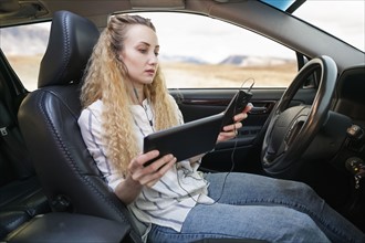 Woman sitting in car and using tablet and mobile phone at same time.