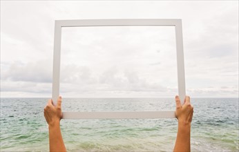 Person holding frame against cloudy sky