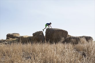 Boy (6-7) walking on bale of hay