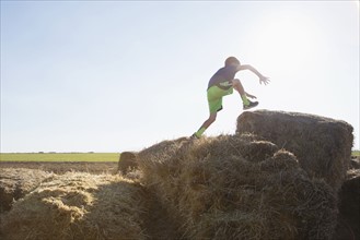 Boy (6-7) jumping on bale of hay