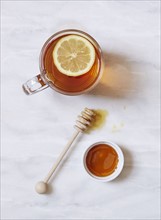 Overhead view of cup of tea with lemon and bowl of honey on marble table