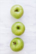 Overhead view of three apples on marble table