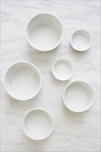 Overhead view of empty white ceramic bowls on marble table