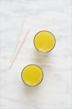Overhead view of glass of orange juice and drinking straws