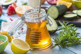 Jar of honey with dipper, lemon and fresh herbs