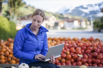 Austria, Salzburger Land, Maria Alm, Mature woman in blue jacket using laptop in market stall