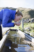 Austria, Salzburger Land, Weissbach, Mature woman drinking water from old wooden drinking trough