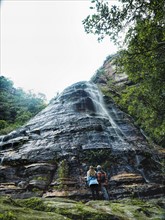 Australia, New South Wales, Blue Mountains National Park, Leura Cascades, Mid-adult couple at foot of rock with waterfall in forest