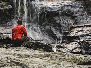 Australia, New South Wales, Blue Mountains, Mid-adult man crouching at foot of waterfall