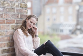 Mid-adult woman sitting and leaning against brick wall