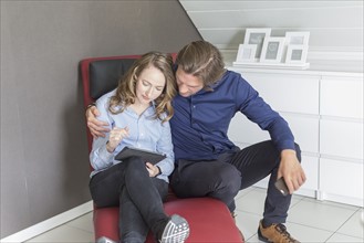 Mid-adult couple sitting on armchair and using tablet
