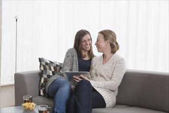 Smiling women sitting on sofa in living room and holding tablet