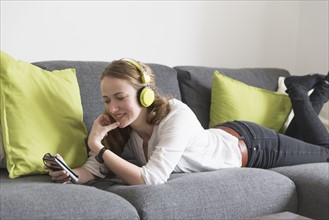 Mid-adult woman lying on sofa and listening to music from smart phone