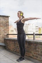 Mid-adult woman exercising on balcony with headphones on