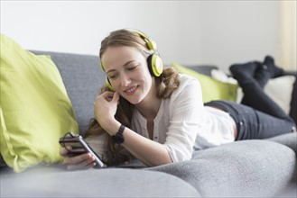 Mid-adult woman lying on sofa and listening to music from smart phone