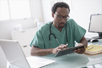 Male doctor working with digital tablet at desk.