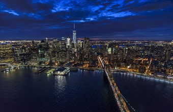 USA, New York, New York City, Manhattan, Aerial view of illuminated skyline with harbor and Brooklyn bridge at night.