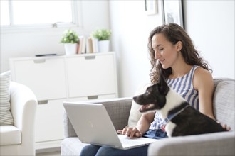 Young woman sitting on sofa with laptop and dog.