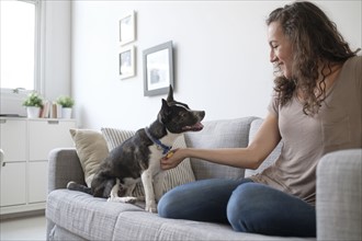 Young woman playing with dog on sofa.