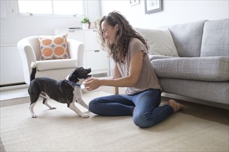 Young woman playing with dog in living room.