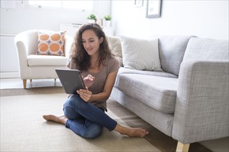 Young woman sitting on floor in living room and using digital tablet.