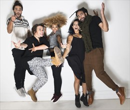 Portrait of group of happy friends against white wall jumping.