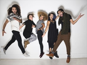 Portrait of group of happy friends against white wall jumping.